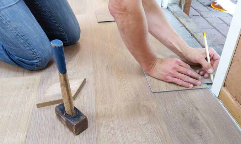 A man kneeling working on restoring an old wooden floor.